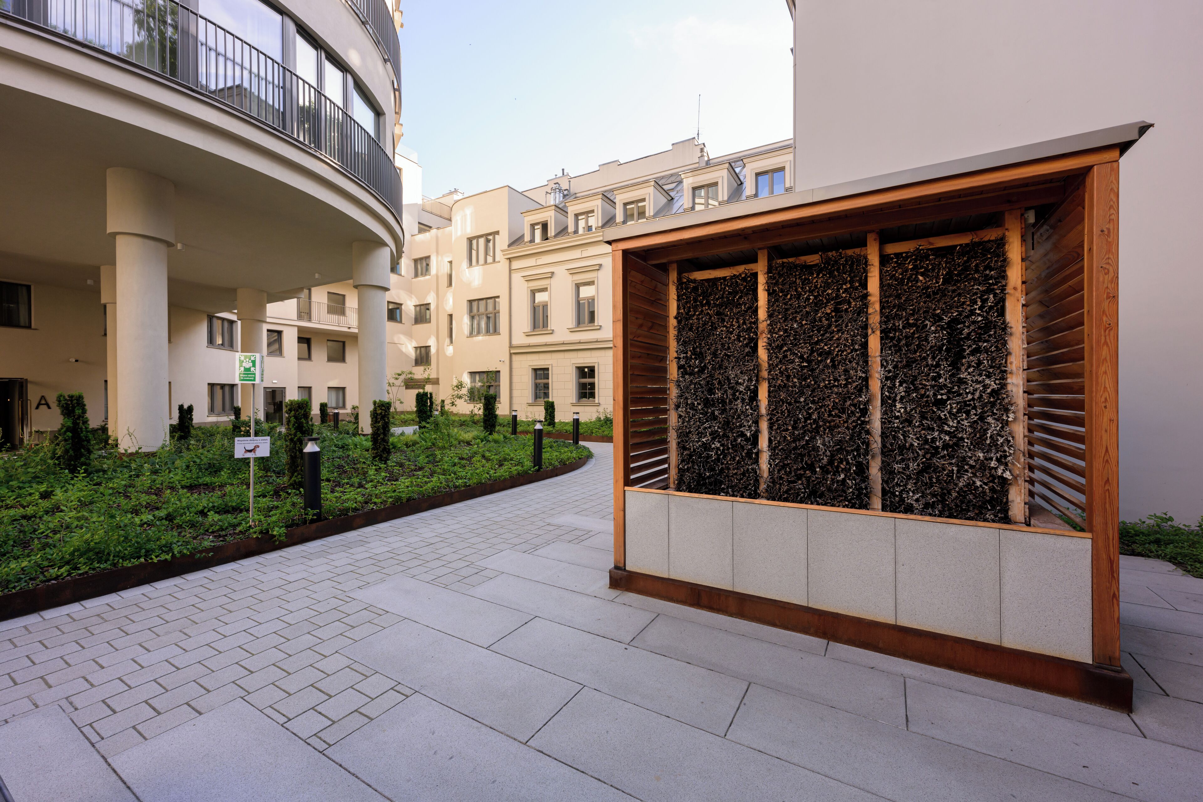 Un edificio moderno con un balcón curvo, un jardín ajardinado y una estructura de madera con fachada decorativa.