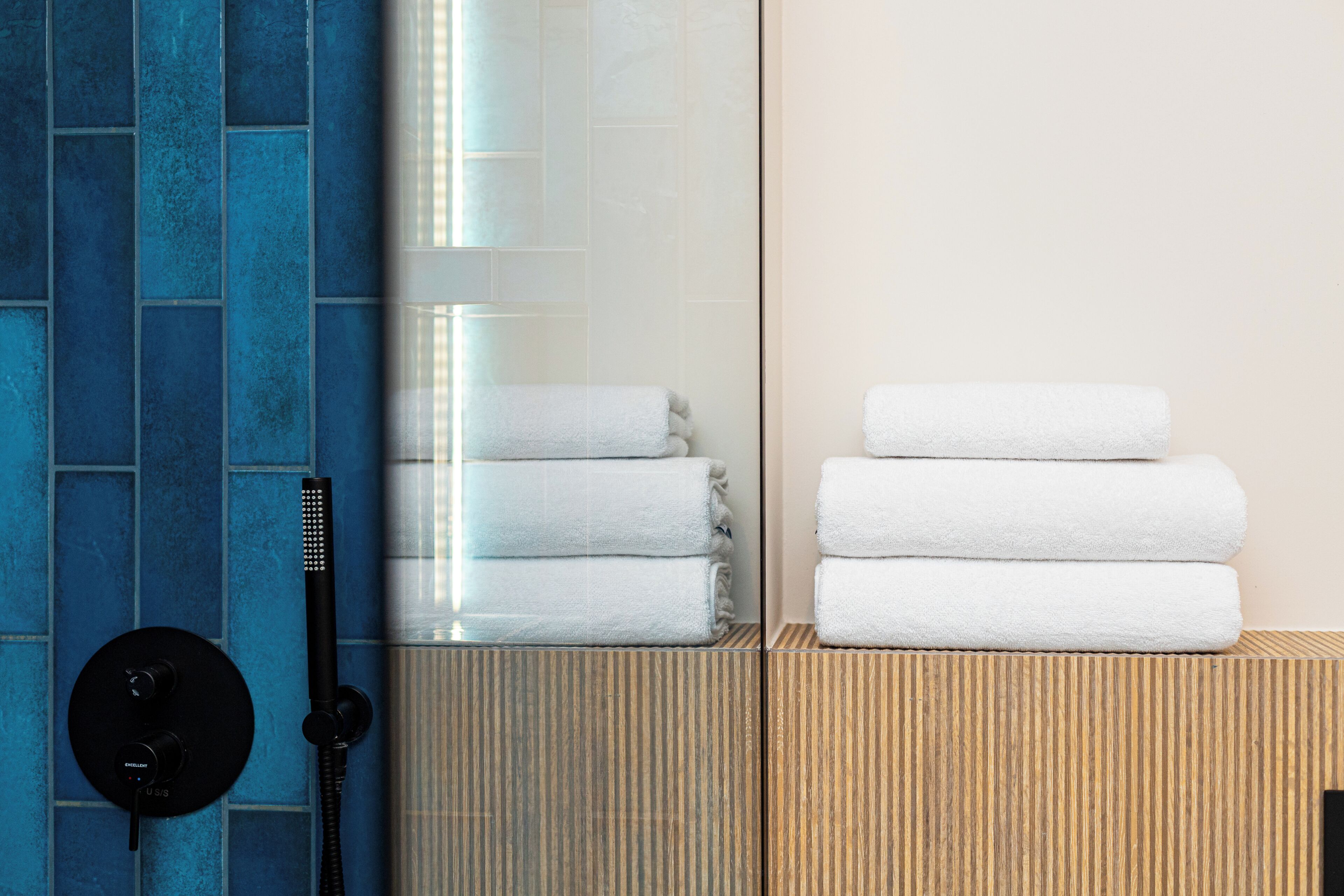 A bathroom with a blue tiled wall, a glass shower enclosure, and a stack of white towels.