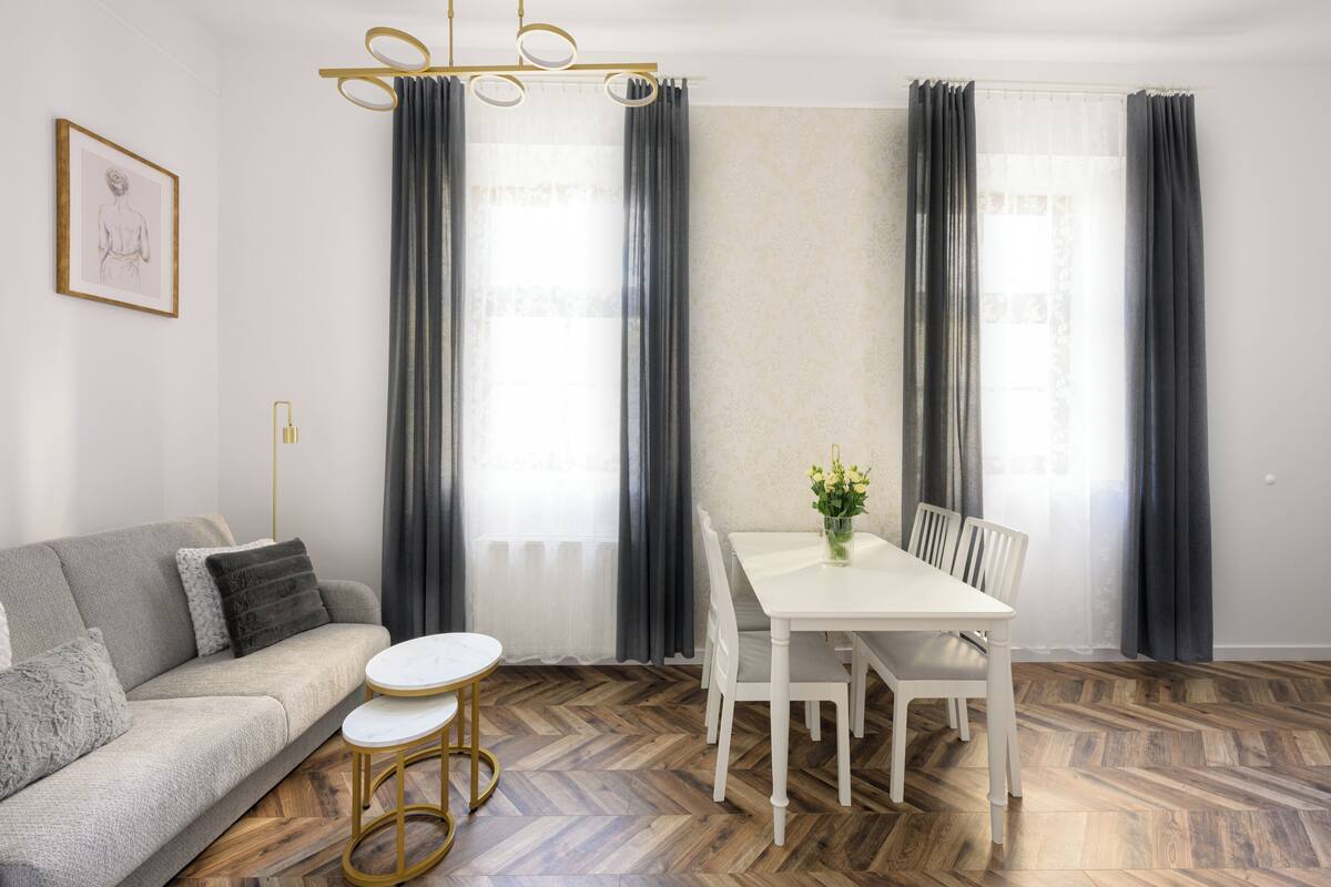 A modern living room with a sofa, a dining table with chairs, and a herringbone wood floor.