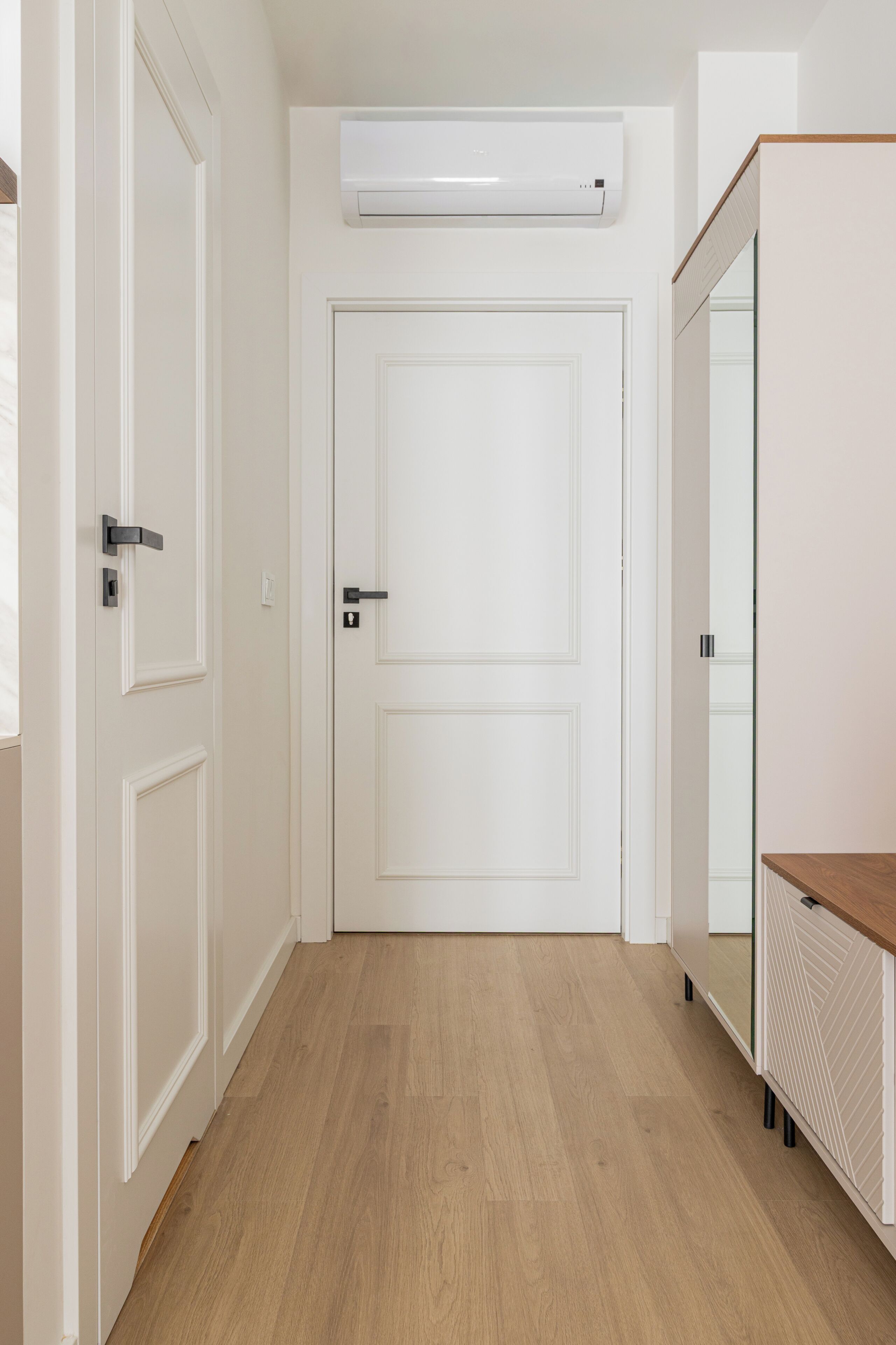 A hallway with a white door, a white radiator, and a wooden floor.