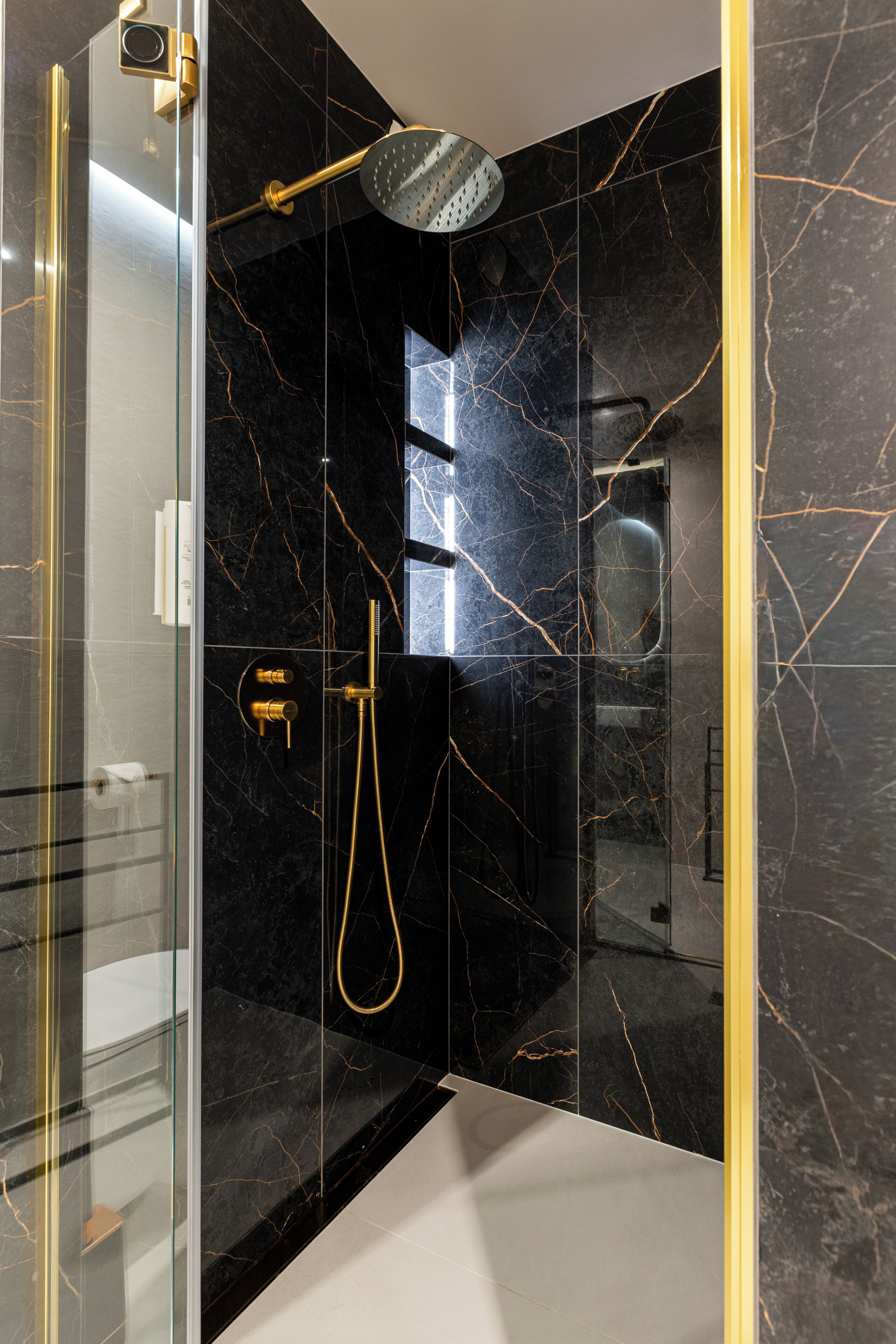 A modern bathroom with a glass-enclosed shower, marble walls, and gold fixtures.