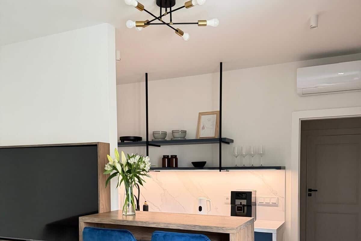 A modern kitchen with a bar area, two blue bar stools, a flat-screen TV, and a ceiling light fixture.