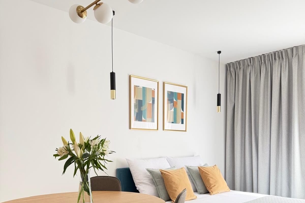 A modern bedroom with a bed, a round dining table, chairs, a vase with flowers, and two abstract paintings on the wall.
