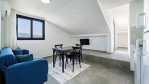 Et moderne køkken med spiseplads, inklusive en blå sofa, et spisebord med stole og et fladskærms-tv monteret på væggen.