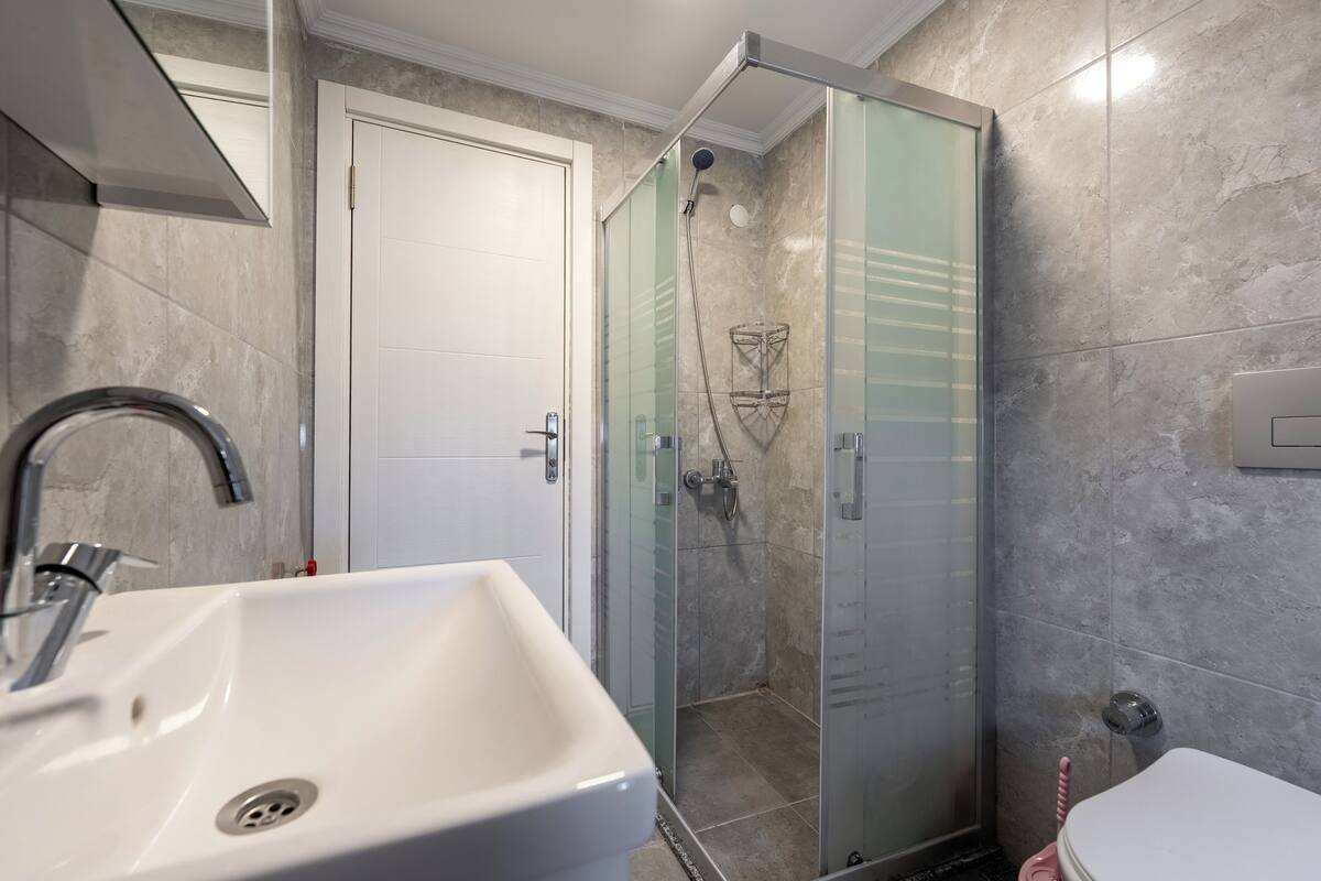 Une salle de bain avec un lavabo blanc, une douche à parois de verre et des toilettes.