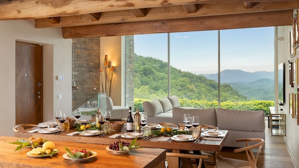 A dining area with a table set for a meal, a stone wall, and a view of a forested landscape. - Villa Krisztina 10 Emma Villas (Bagnone)