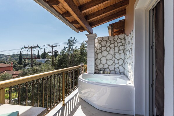 A balcony with a stone wall, a hot tub, and a view of the surrounding area.