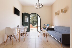 Een moderne woonkamer met een grijze bank, witte stoelen, een eettafel en een aan de muur bevestigde televisie.