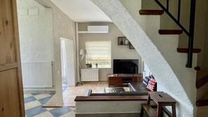 Una sala de estar con televisión, sofá y escalera.