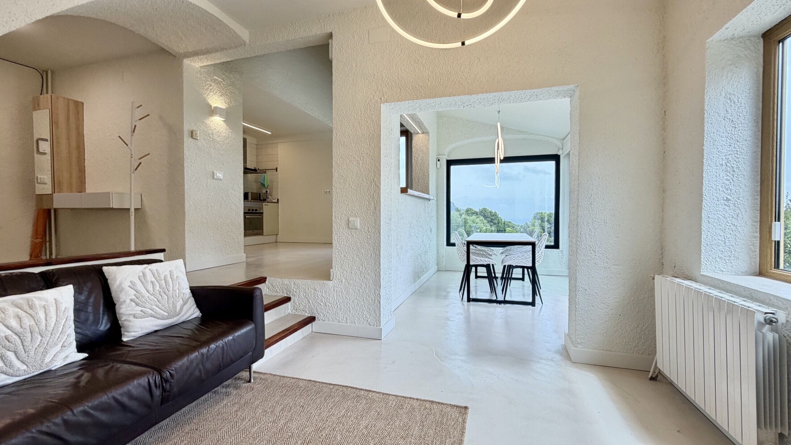 Una sala moderna con un sofá de cuero, un comedor con mesa y sillas, y vista a través de un arco hacia una cocina y comedor.
