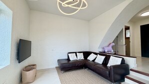 A modern living room with a sectional sofa, a flat-screen TV, and a unique circular light fixture.