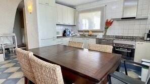 Une cuisine moderne avec un coin repas, comprenant une table en bois, des chaises en osier et un four encastré.