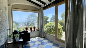 A room with a checkered floor, a table with potted plants, a chair, and large windows with curtains.