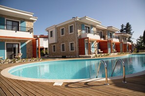 A swimming pool with a wooden deck, a stone facade building, and a blue sky. - Eski Kapı Datça  (Datça)