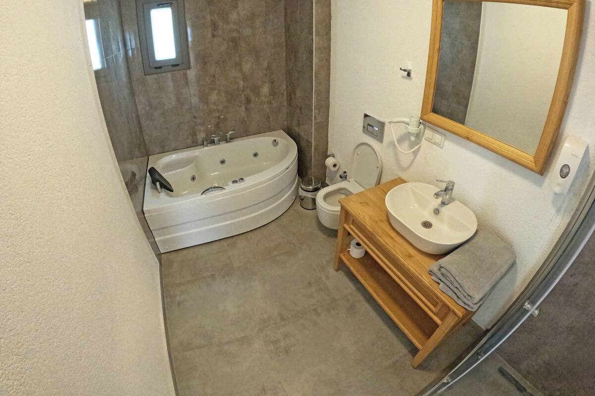 A modern bathroom with a freestanding bathtub, a toilet, and a sink with a mirror above.