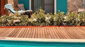 A poolside area with a wooden deck, a stone wall, and a door with blue shutters.