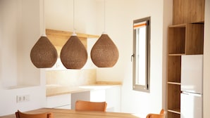 A modern kitchen with a wooden table and chairs, hanging woven light fixtures, and a built-in wooden shelf unit.