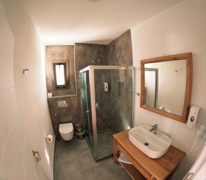 A bathroom with a toilet, a glass-enclosed shower, and a wooden vanity with a sink. - Eski Kapı Datça  (Datça)