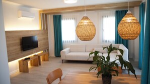 A modern living room with a flat-screen TV, wooden benches, a dining table, and a potted plant.
