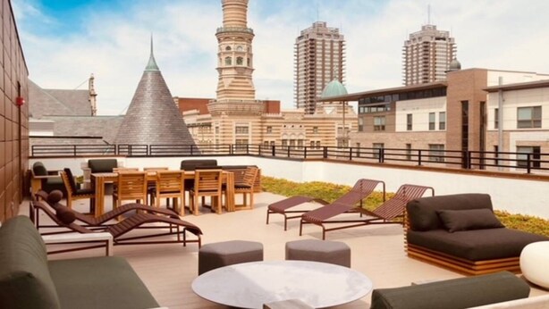 Terraza en la azotea con mobiliario exterior, incluyendo sillones de descanso y una mesa, con vistas a un paisaje urbano con edificios modernos y una mezquita.
