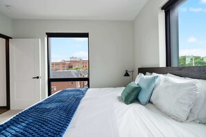 A bedroom with a large bed, a window, and a view of buildings outside.