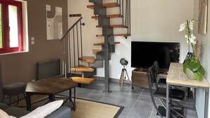 A modern living room with a staircase, a flat-screen TV, and a dining area. - Cosy sur Ourcq (TROESNES)