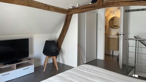 A modern room with exposed wooden beams, a flat-screen TV on a wooden stand, a black chair, and a staircase with a metal railing. - Cosy sur Ourcq (TROESNES)