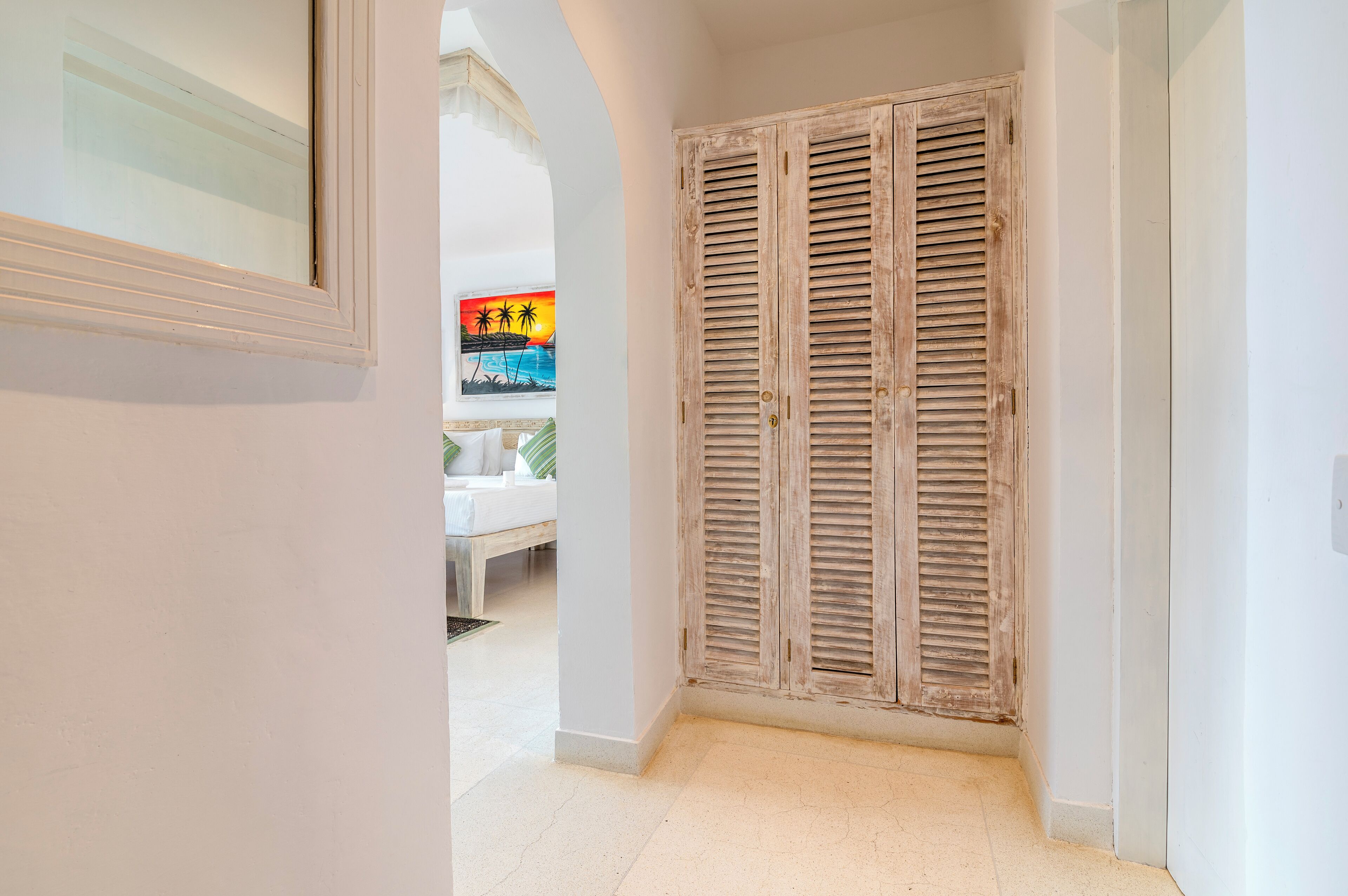 A hallway with a wooden door and a painting of a sunset.