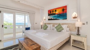 A bedroom with a large bed, a wooden bench, a nightstand, and a painting of a sunset over the ocean. - Amani Beachfront Villa by YourHost (Watamu)