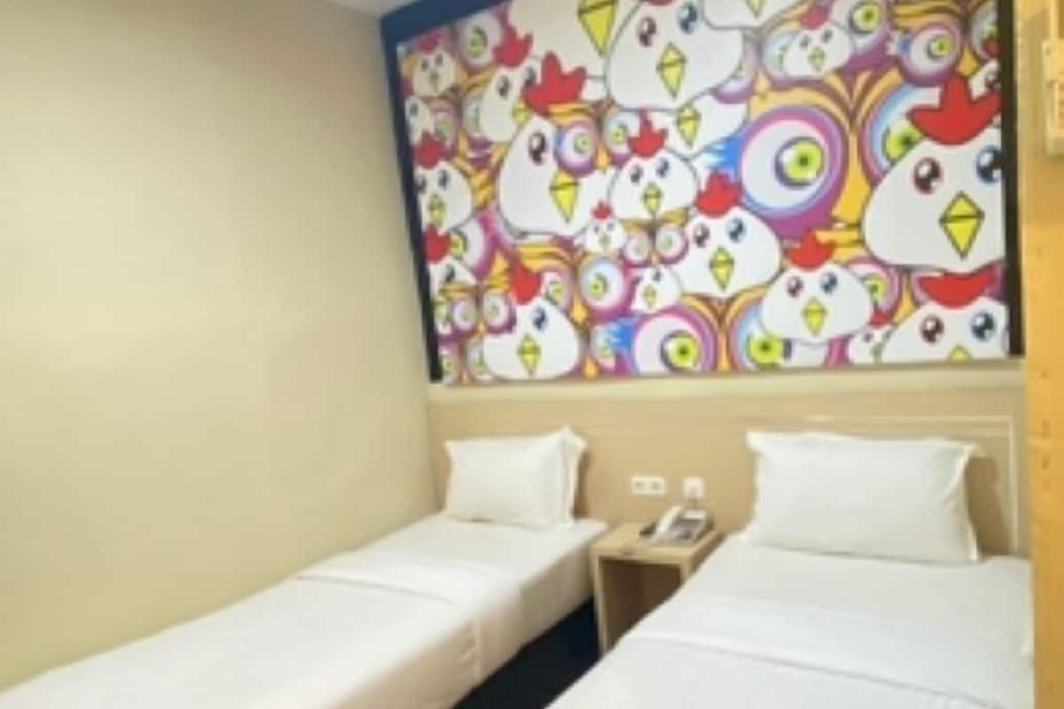 Ein Hotelzimmer mit zwei Einzelbetten, einem farbenfrohen Wandbild und Holzboden.