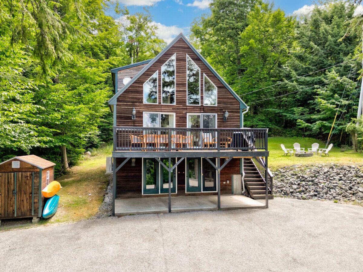 A two-story cabin with a balcony, a small shed, and outdoor seating.