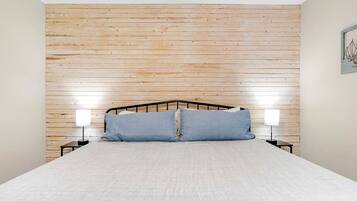 A bedroom with a wooden slat headboard, a bed with white bedding, two bedside tables with lamps, and a framed picture on the wall.