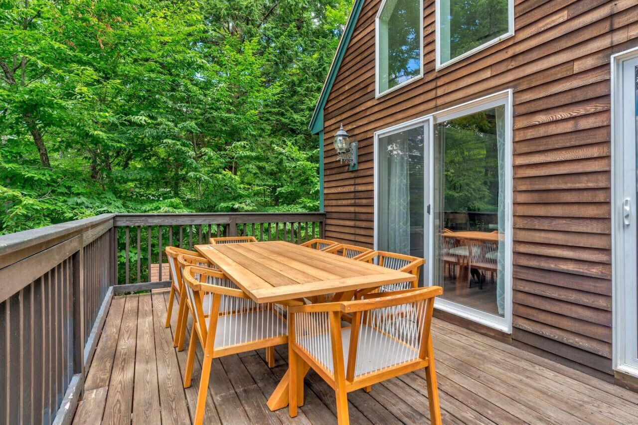 A wooden deck with a table and chairs, surrounded by lush greenery.