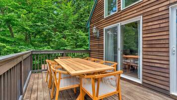 A wooden deck with a table and chairs, surrounded by lush greenery.