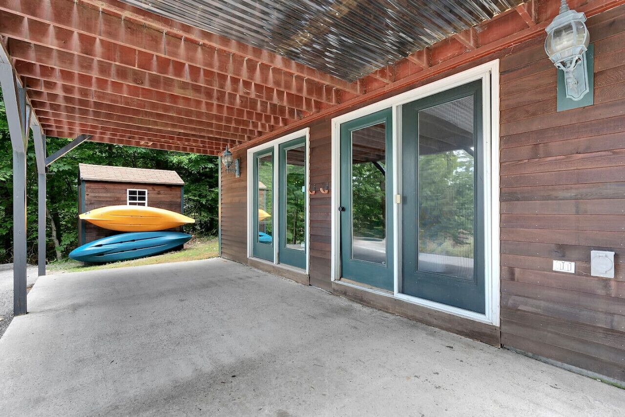 A covered outdoor area with a wooden building, large sliding glass doors, and kayaks stored outside.