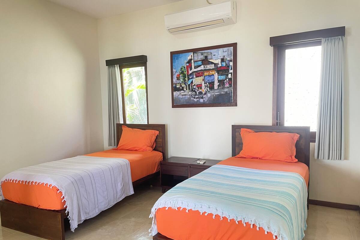 Une chambre d’hôtel avec deux lits simples, une table de chevet, un appareil de climatisation et un tableau au mur.
