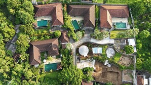 An aerial view of a residential area with multiple houses, each featuring a swimming pool, surrounded by lush greenery. - Ponjok Batu Residence (Tejakula)