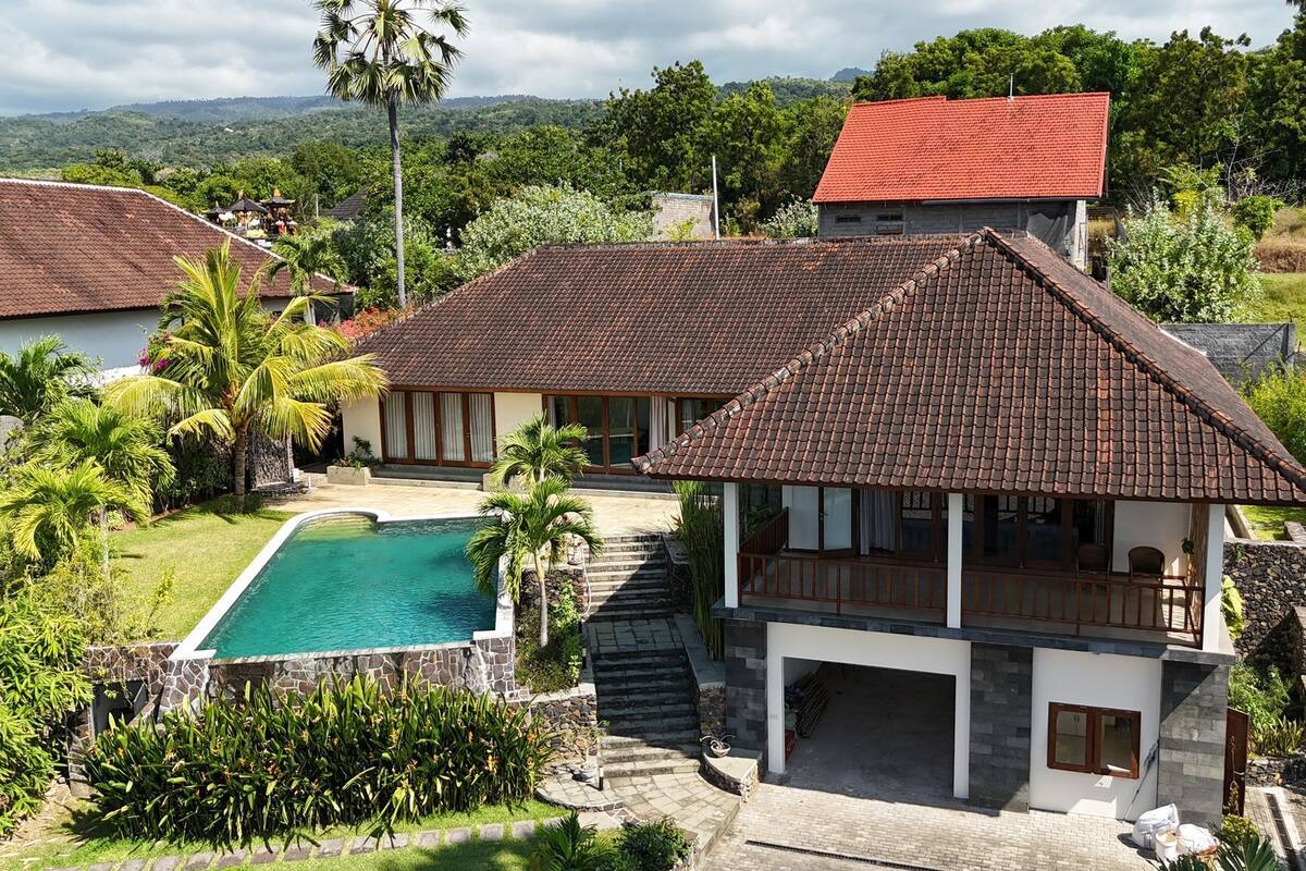 Une villa dotée d’une piscine, entourée d’une végétation luxuriante et offrant une vue sur un paysage montagneux.