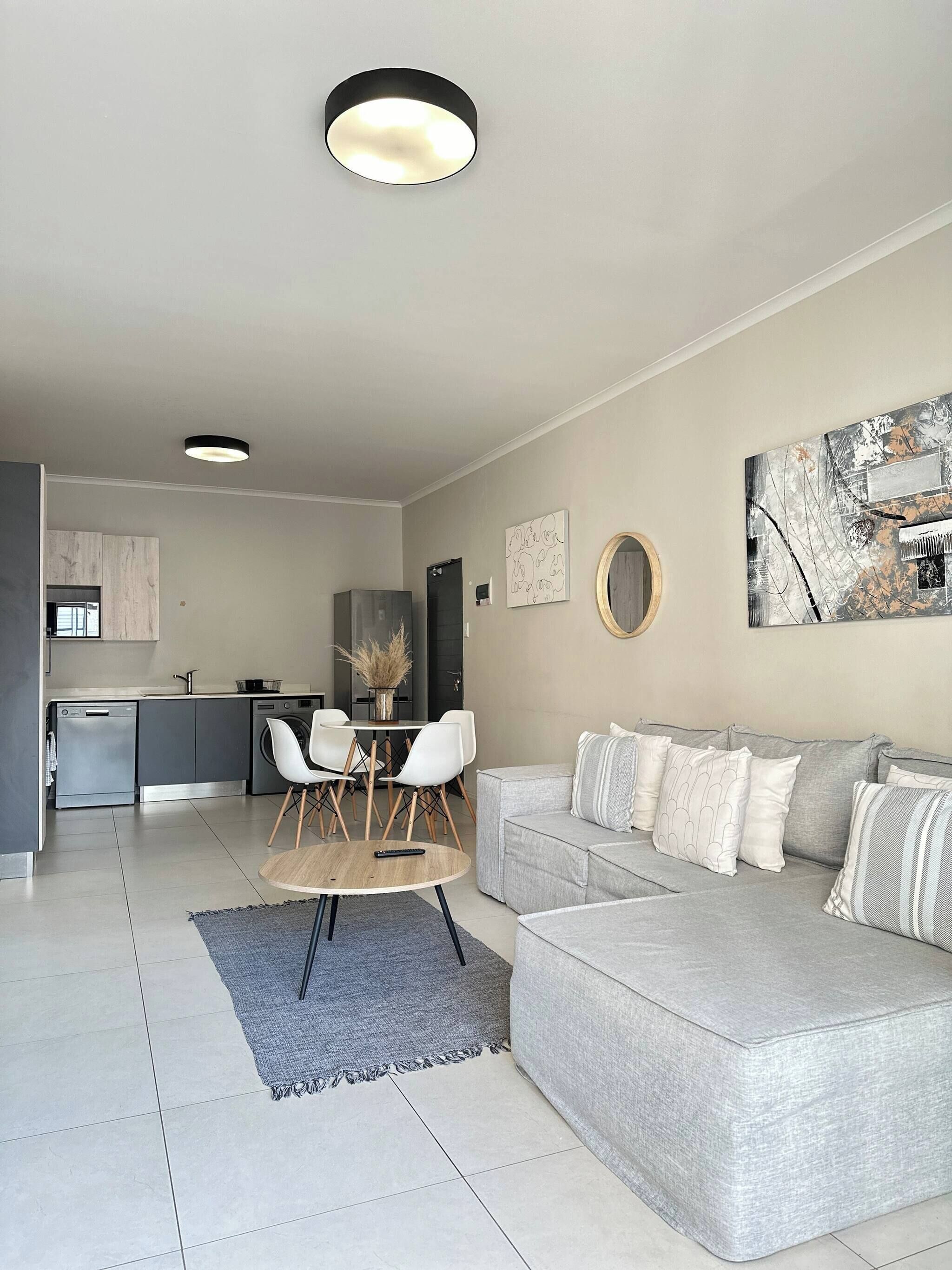 Una sala de estar moderna con un sofá gris, una mesa de comedor con sillas y una cocina al fondo.