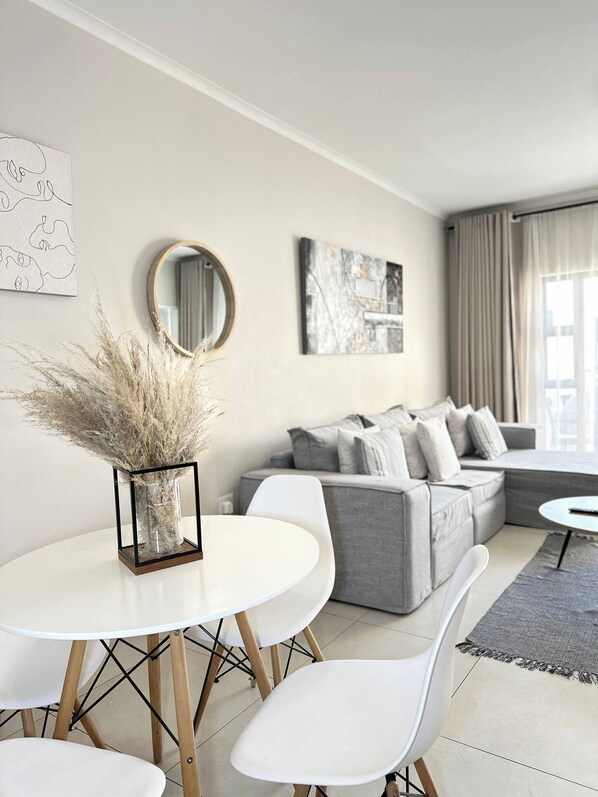 Relax in this stylish living room with a round dining table, comfortable sofa, and large window.