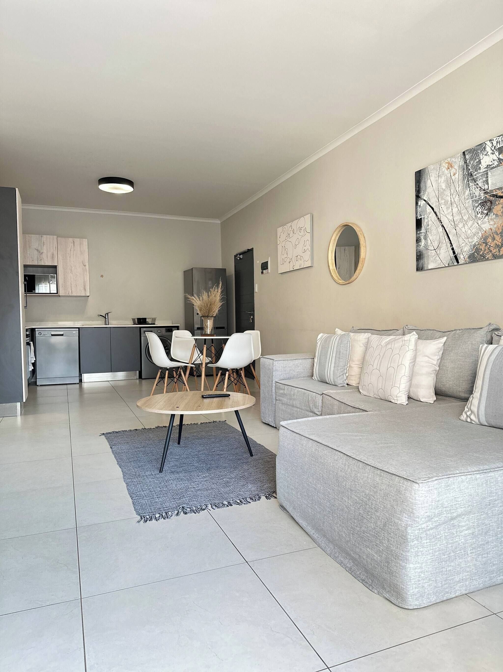 A modern living room with a grey sofa, a dining table with chairs, and a kitchen in the background.