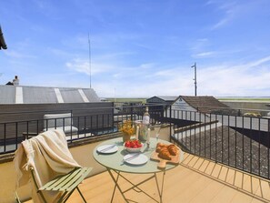 Een terras op het dak met een tafel voor twee personen, inclusief een champagnefles, een fruitschaal en croissants.