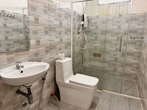 Un baño con lavamanos, inodoro y ducha con mampara de vidrio.