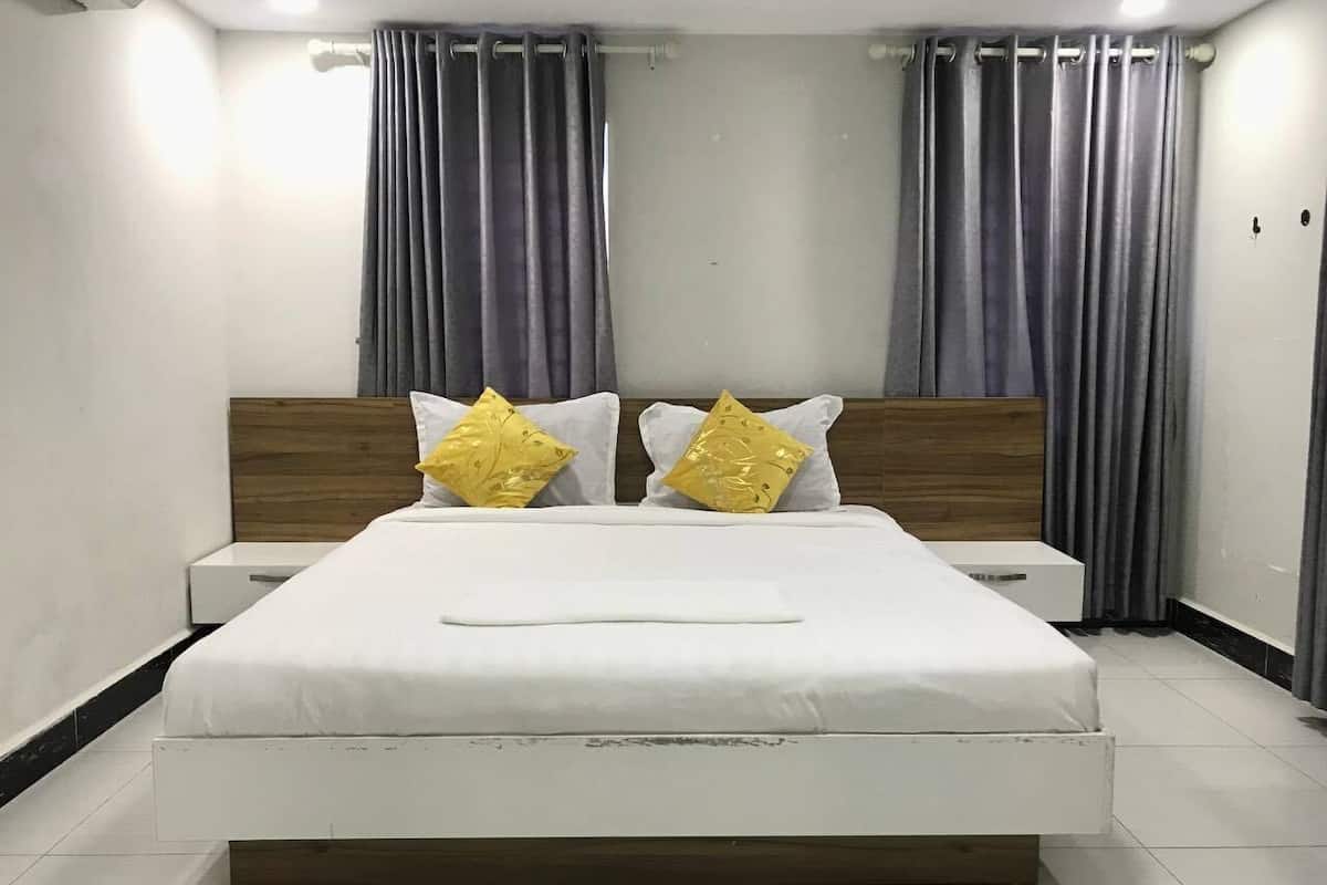 A neatly made bed with white bedding and two pillows, a wooden headboard, and a nightstand with a small table.