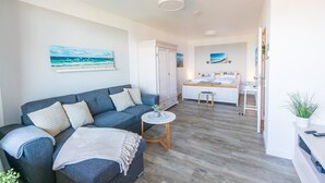 Un salón moderno con un sofá gris, una mesita redonda y una cama al fondo.