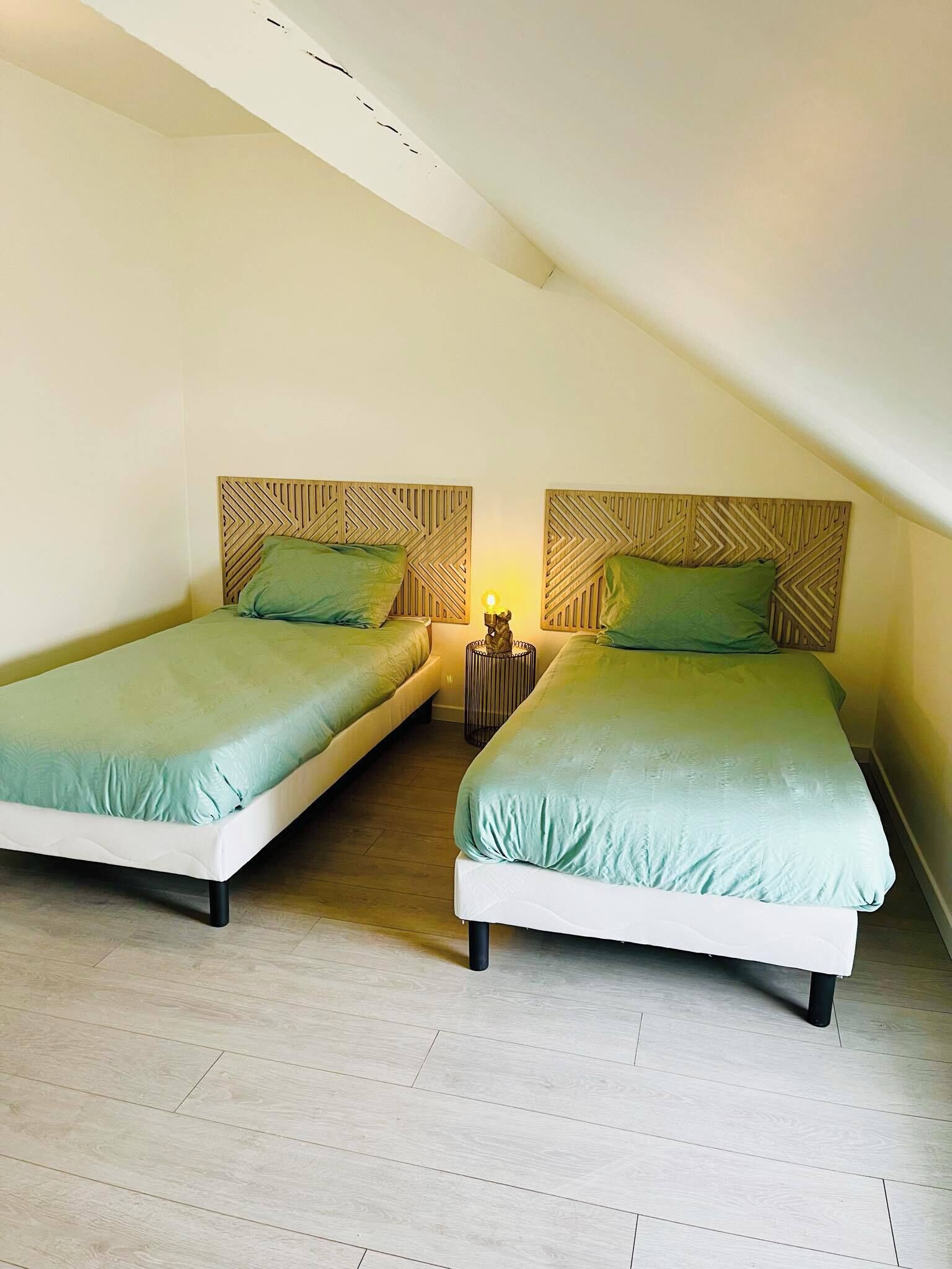 Une chambre avec deux lits, chacun doté d’une tête de lit en bois et d’une literie verte.