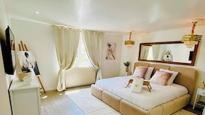 Un dormitorio con una cama grande, una mesita de noche, un aparador, un espejo y una ventana con cortinas.