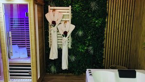 Un cuarto de spa con una sauna de madera, una camilla de masaje y una pared cubierta de follaje verde.