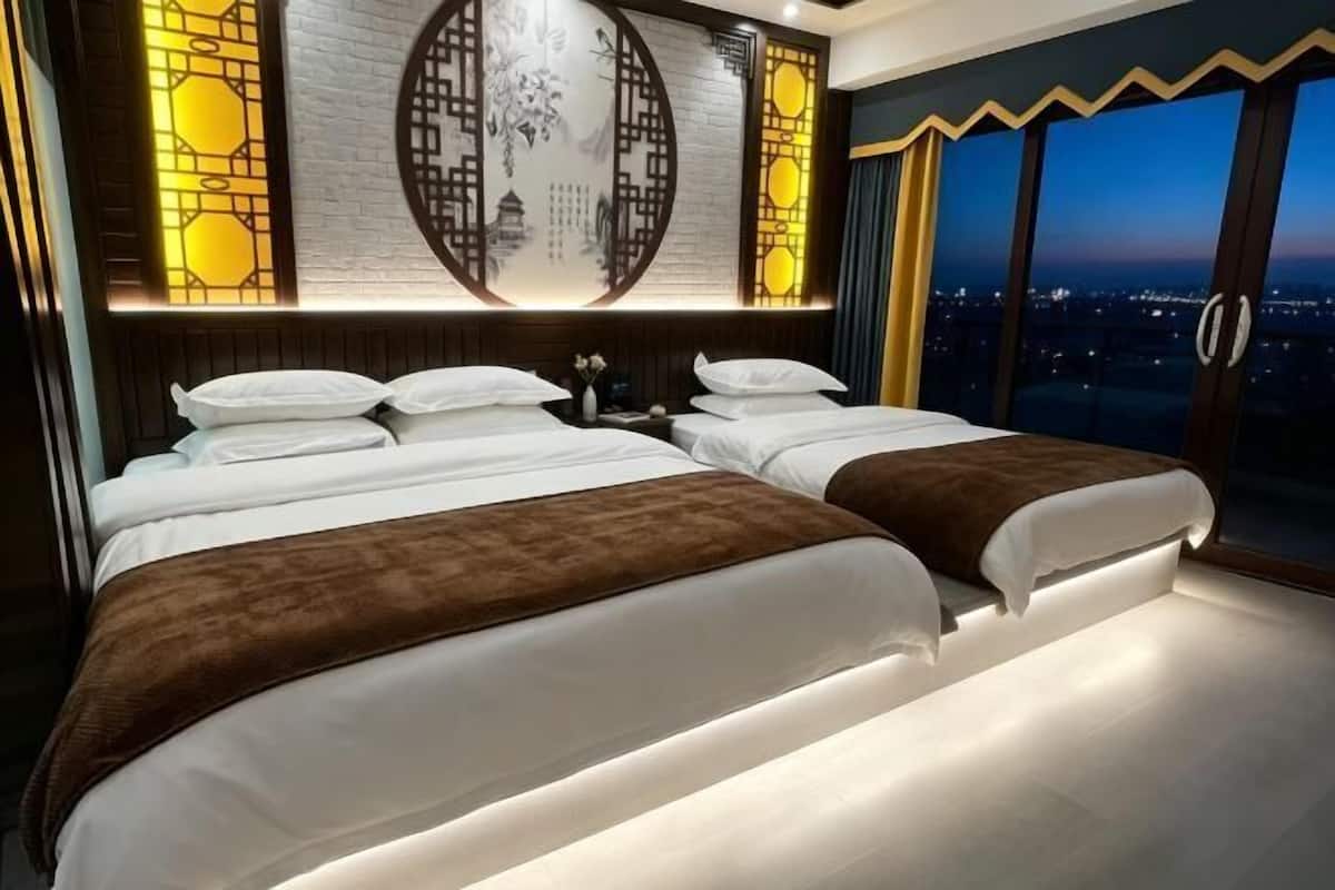 Ein Hotelzimmer mit zwei Betten, einem großen Fenster und Blick auf die Stadt sowie dekorativen Wandverkleidungen.