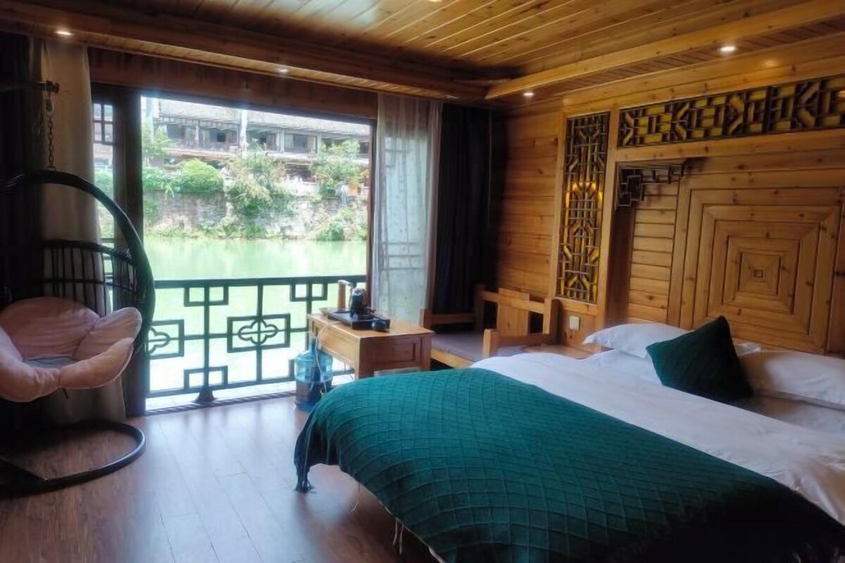 A wooden room with a bed, a chair, and a view of greenery outside.